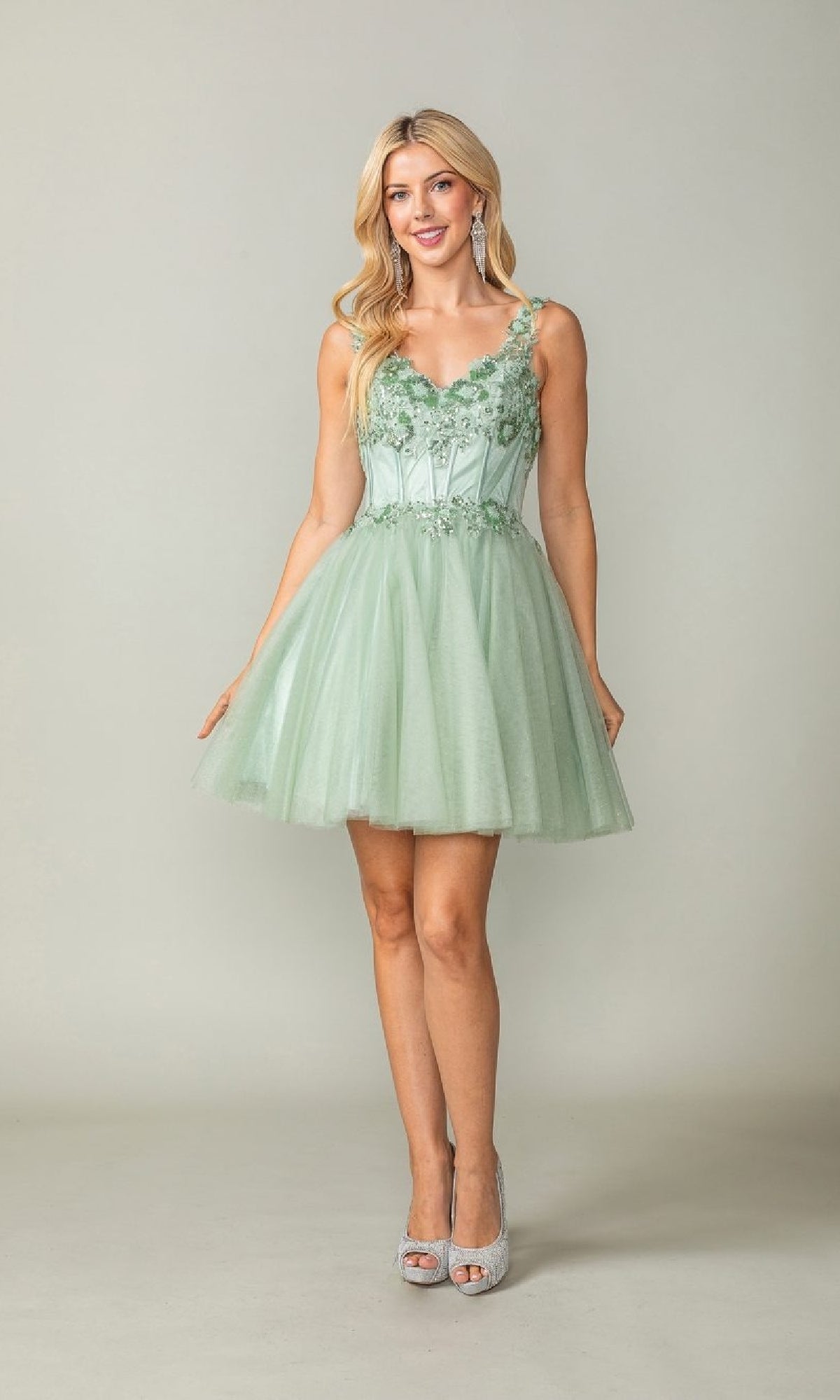 Woman wearing a light green dress with floral embellishments on a plain background
